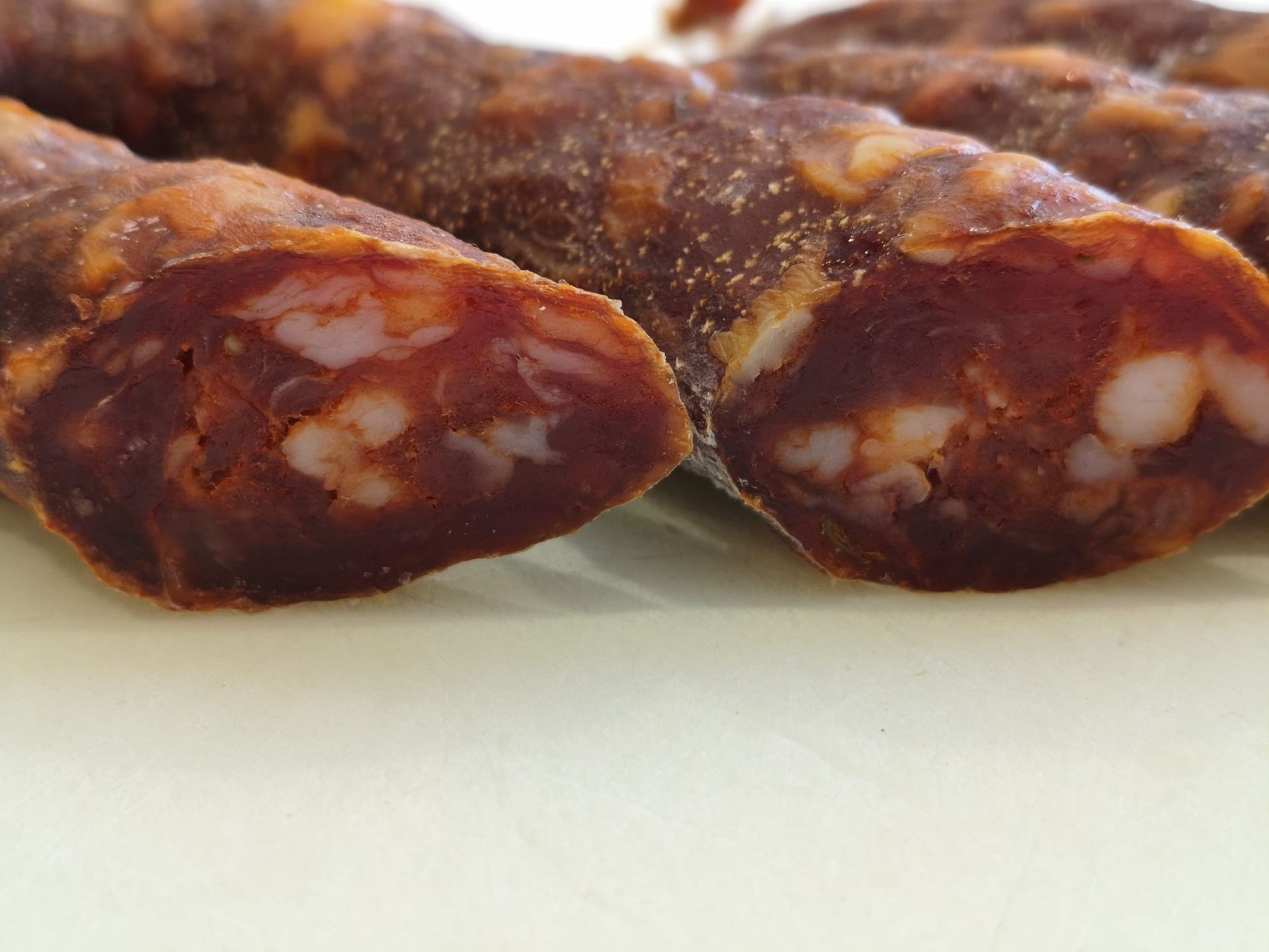 Salumi stagionati appesi su rastrelliere, etichettati con i prezzi, contro una parete piastrellata.