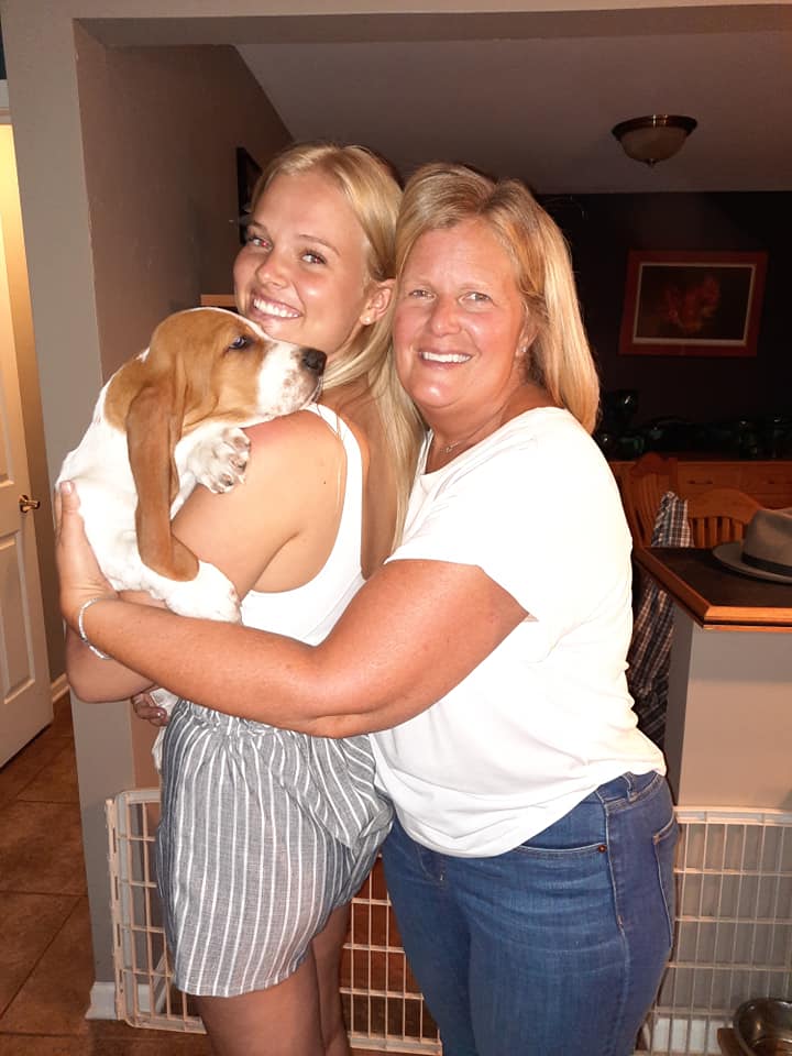 Two women are hugging a dog in a living room.