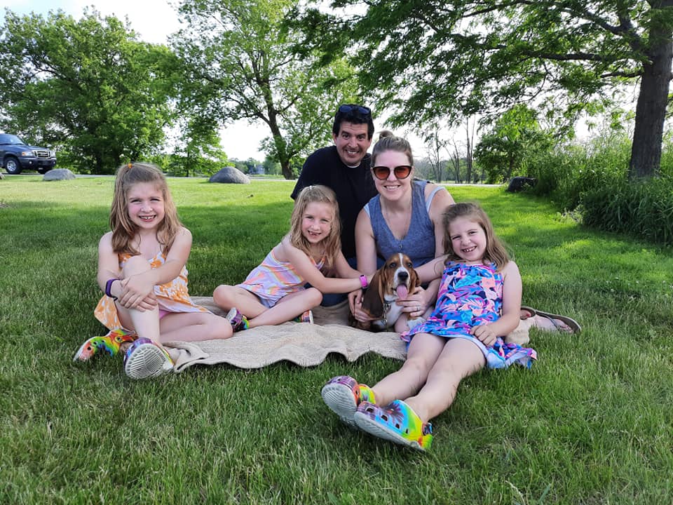 A family is sitting on a blanket in the grass with a dog.