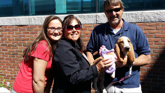 A man and two women are holding a dog in front of a brick wall.