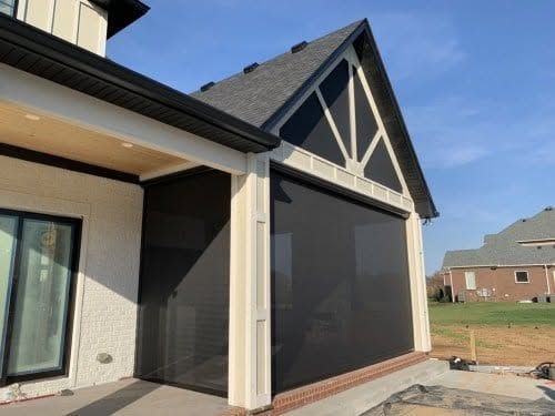 Covered patio with dark mesh screens and beige trim on a house exterior under a blue sky