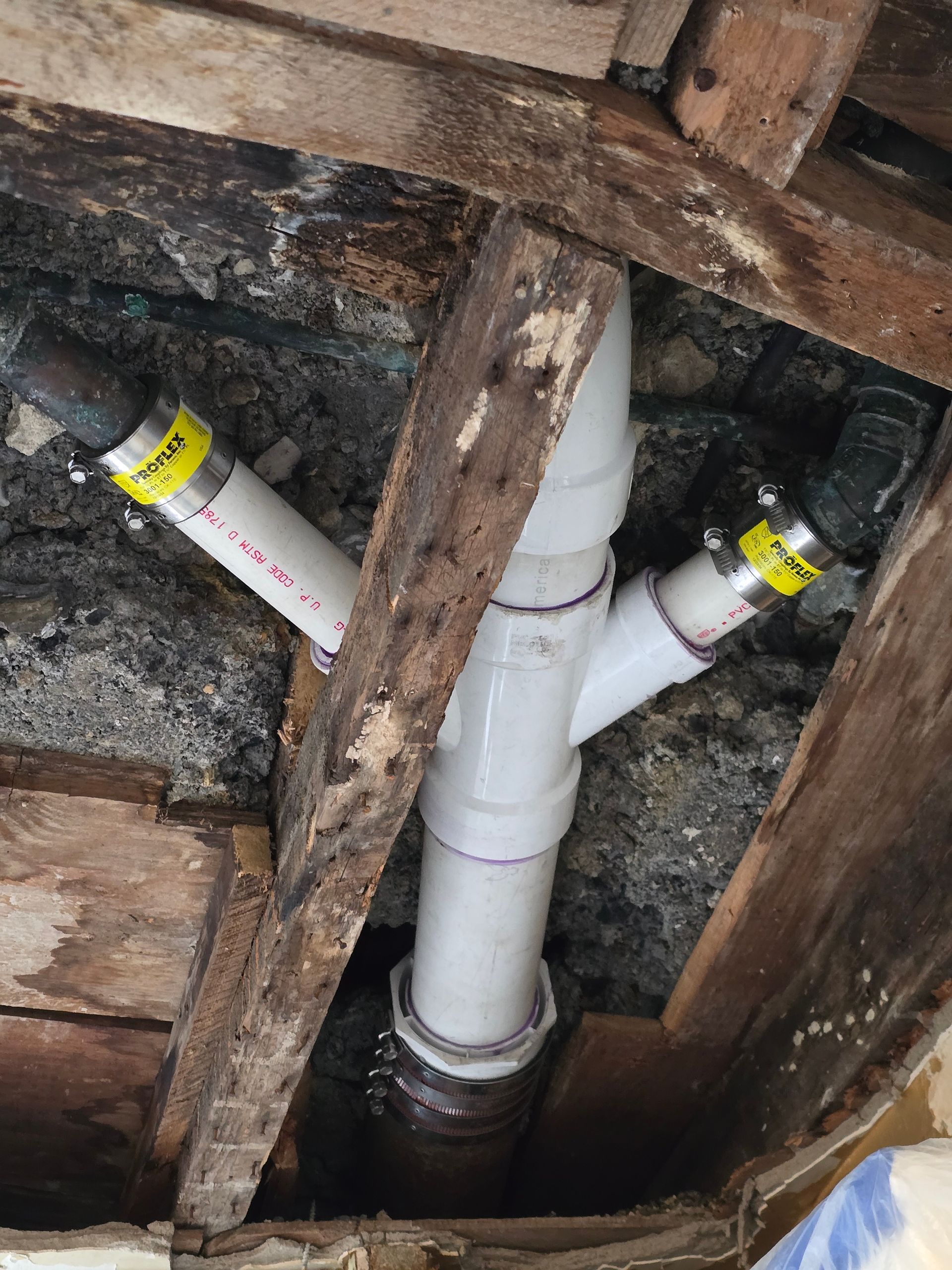White PVC plumbing pipes with two inlets and one outlet, in an exposed ceiling with wooden beams.