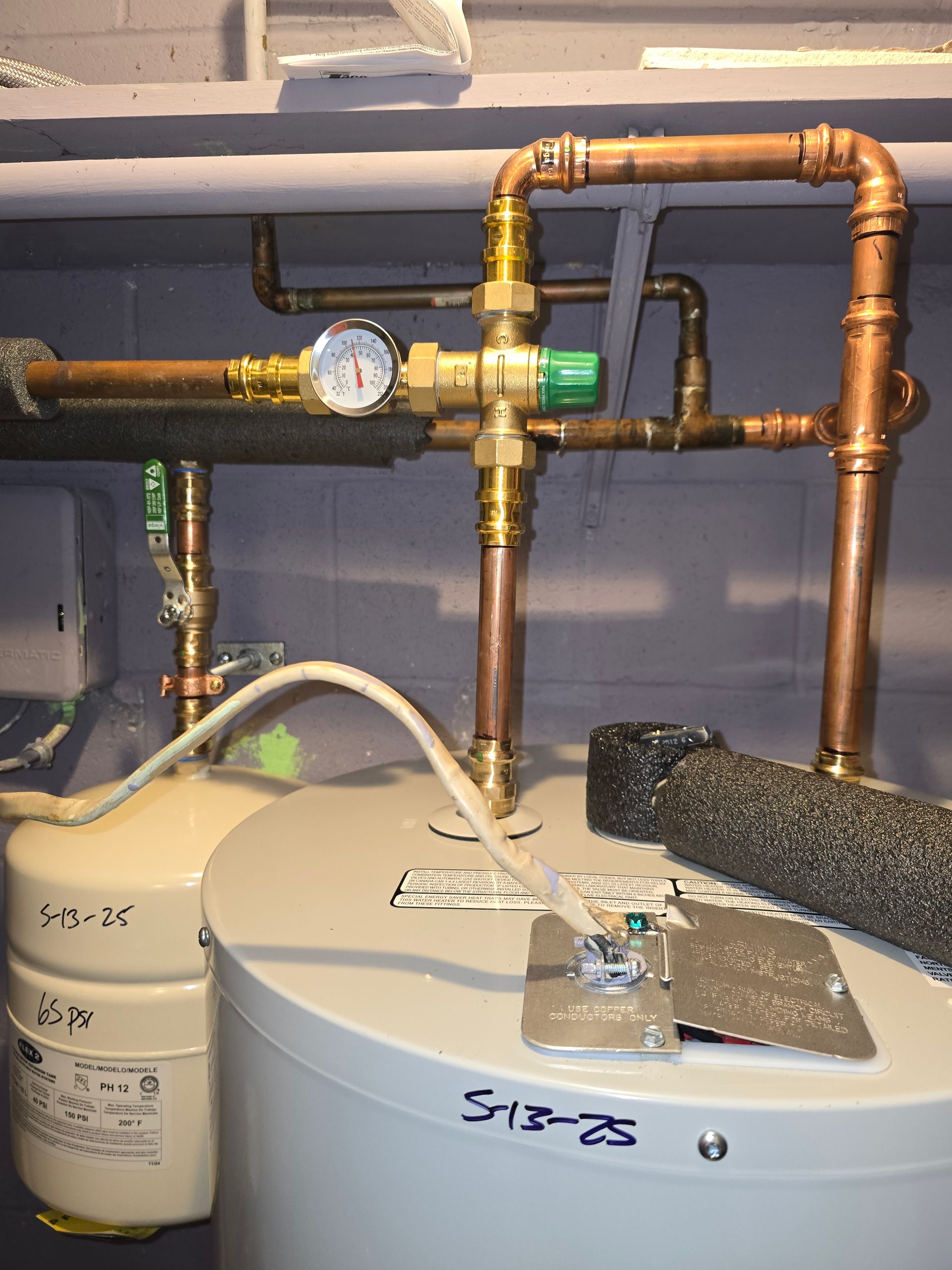 Two water heaters with copper pipes, a pressure gauge, and an expansion tank in a utility room.