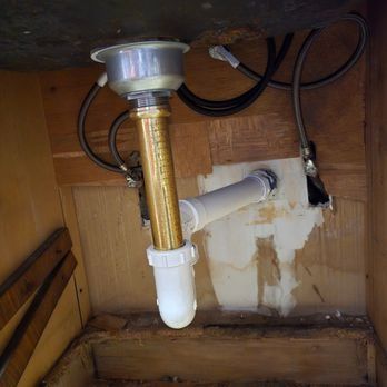 Underside of a sink with plumbing. A shiny gold drain pipe connects to white PVC drain pipes.