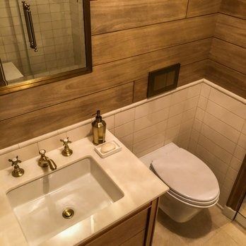 Bathroom with wood-paneled walls, white toilet, marble vanity with gold fixtures, and a mirror.