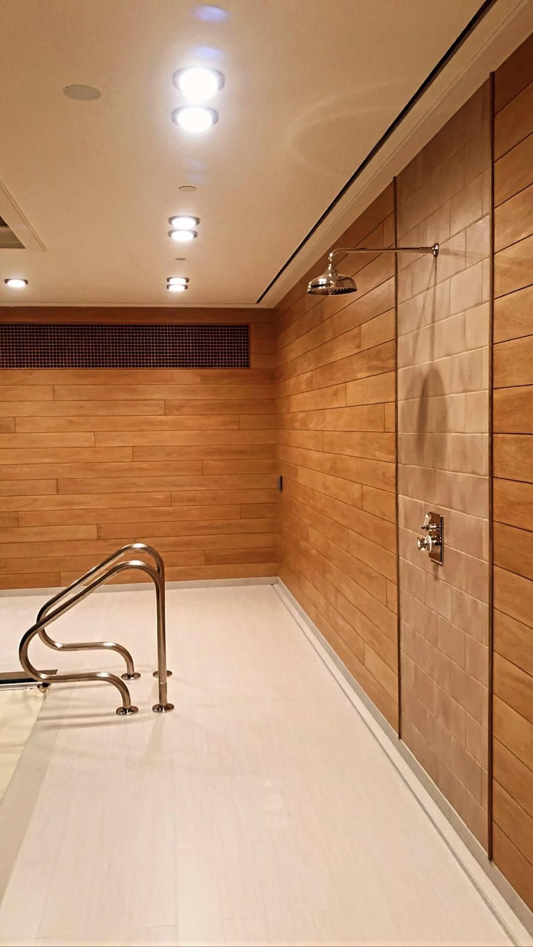 Shower area with light wood paneling, white floor, and stainless steel fixtures.