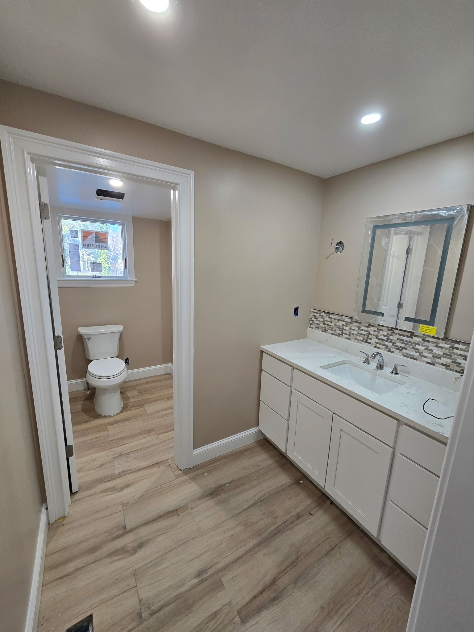 Bathroom with white vanity, toilet, beige walls, and wood-look tile flooring.