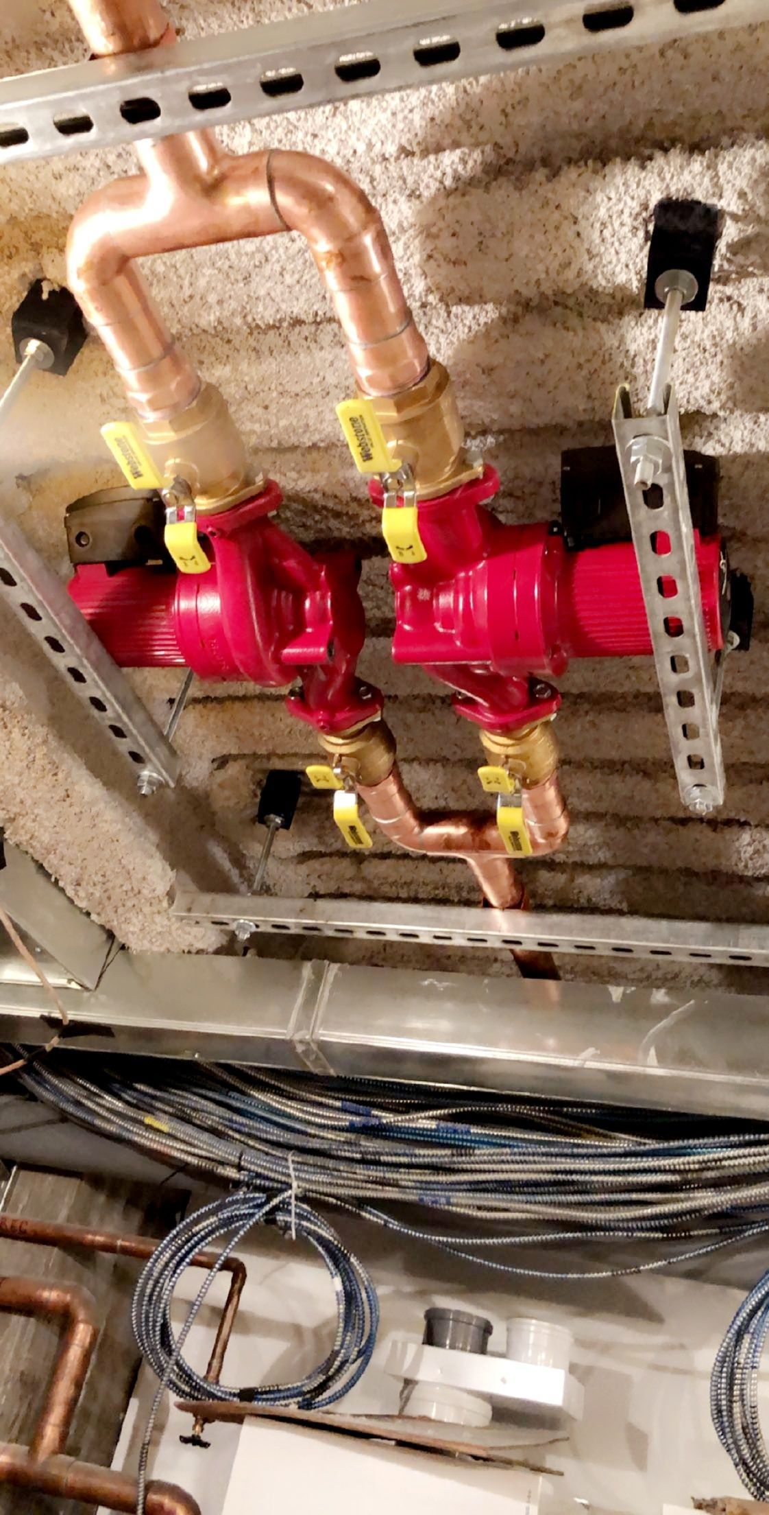 Two red pumps with copper pipes, yellow valves, and metal supports in a ceiling.