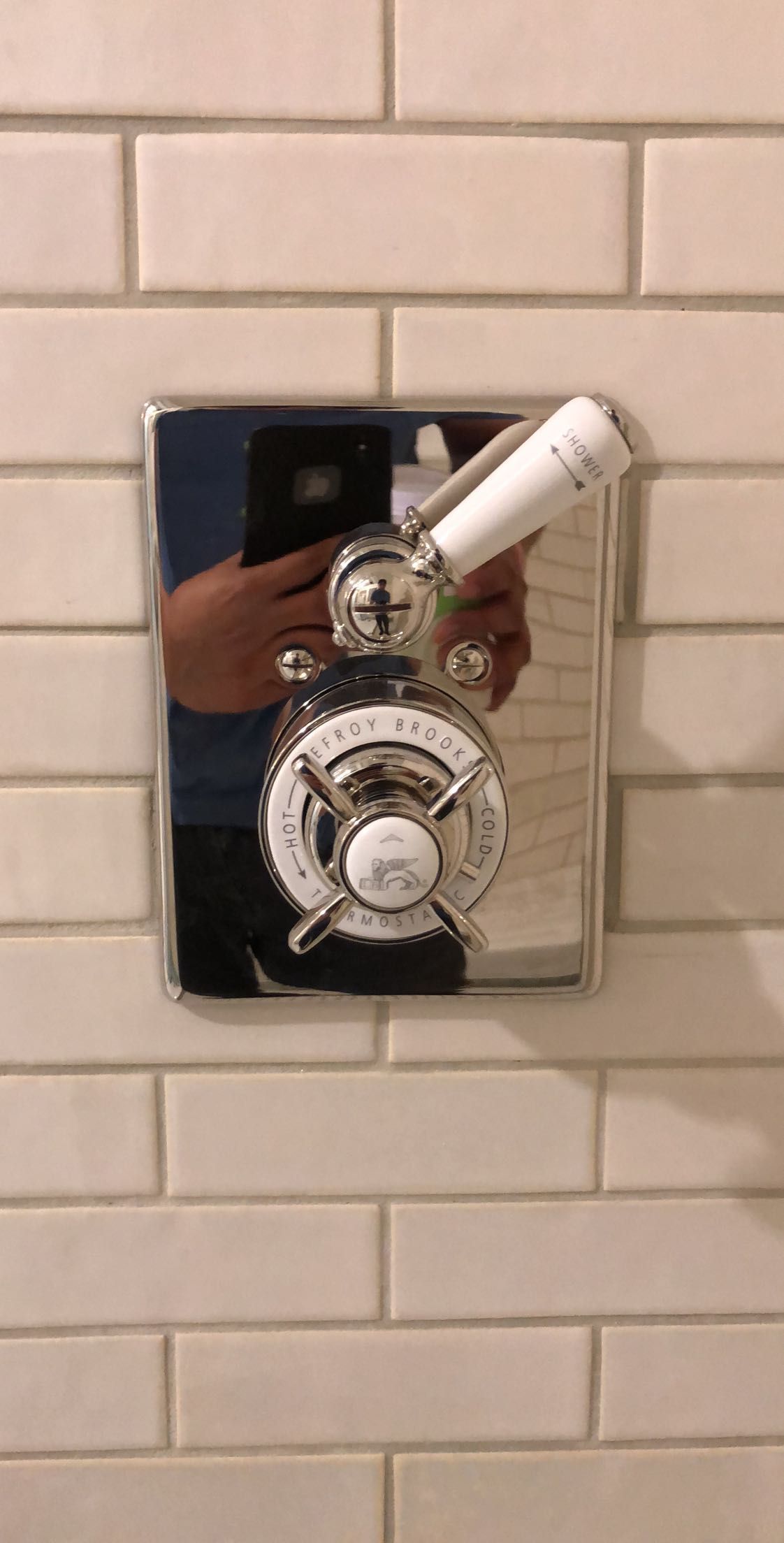 Chrome shower valve with white levers, mounted on white brick tile wall.