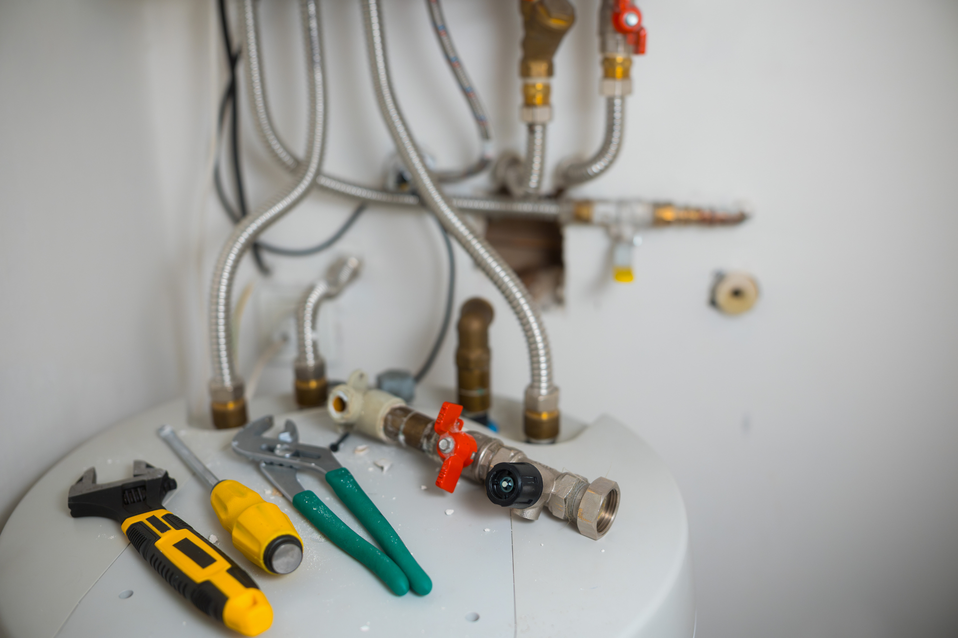 Plumbing tools on top of a water heater with pipes and connections.