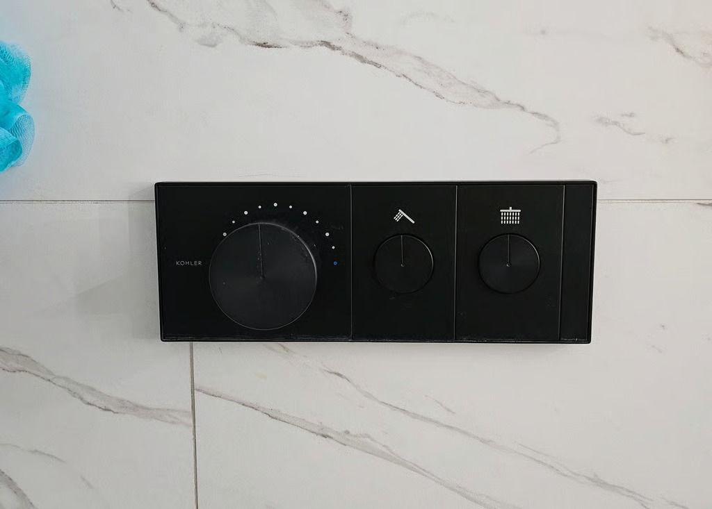 Black shower control panel with three dials on a marble wall.