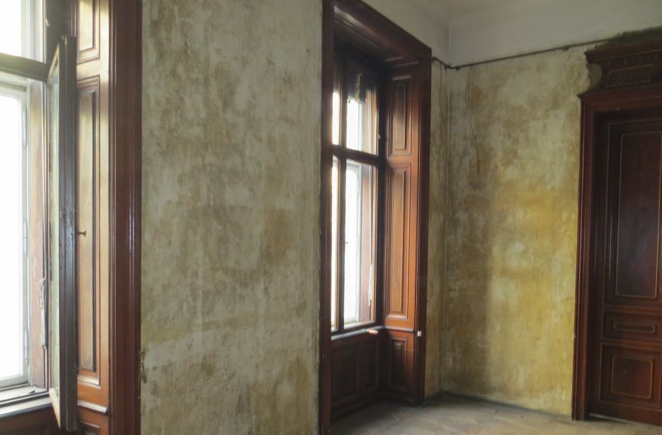 Ein leerer Raum mit zwei Fenstern und einer Tür.