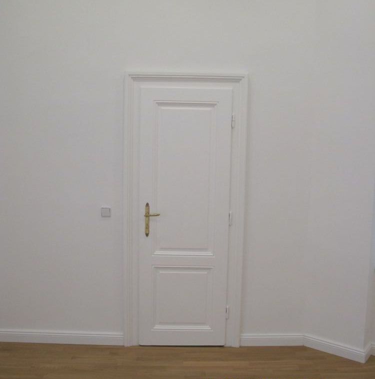 Ein leerer Raum mit einer weißen Tür und Holzboden.