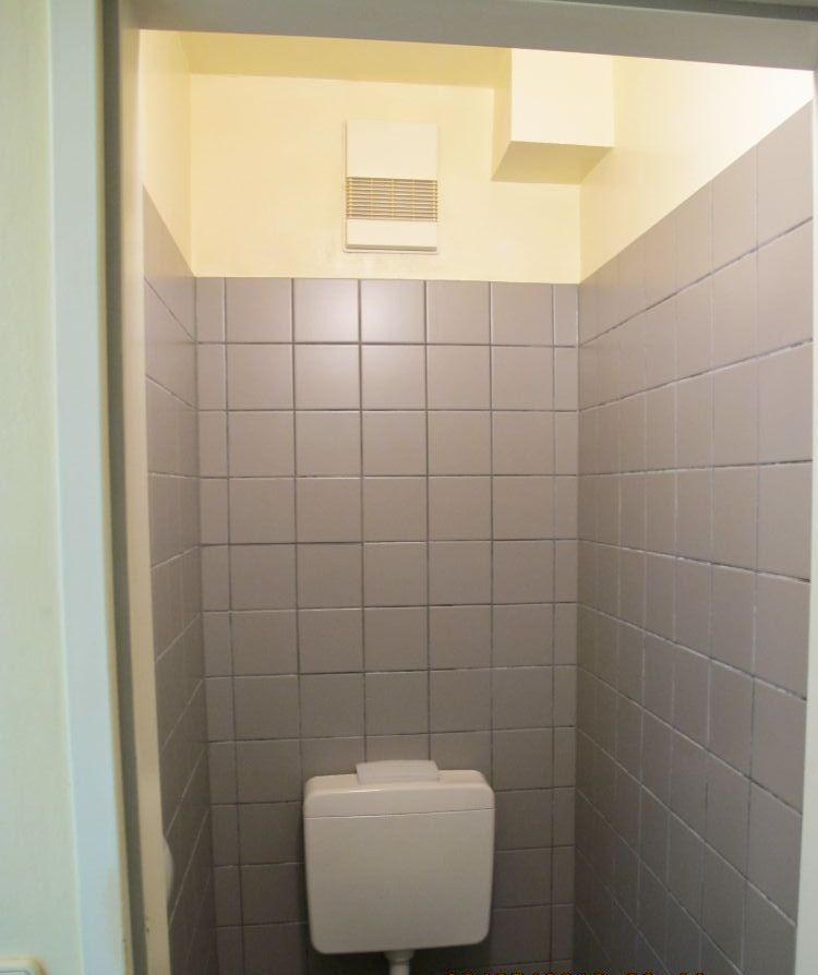 Ein Badezimmer mit grauen Fliesen und einer Toilette