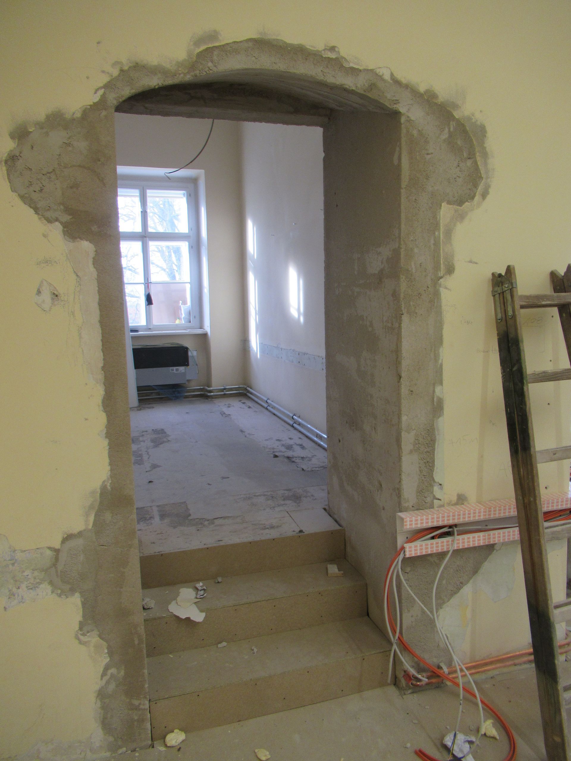 In einem Raum lehnt eine Leiter an einer Wand neben einer Tür.