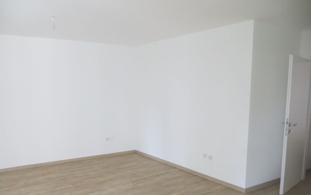 Ein leerer Raum mit weißen Wänden, Holzboden und einer Tür.