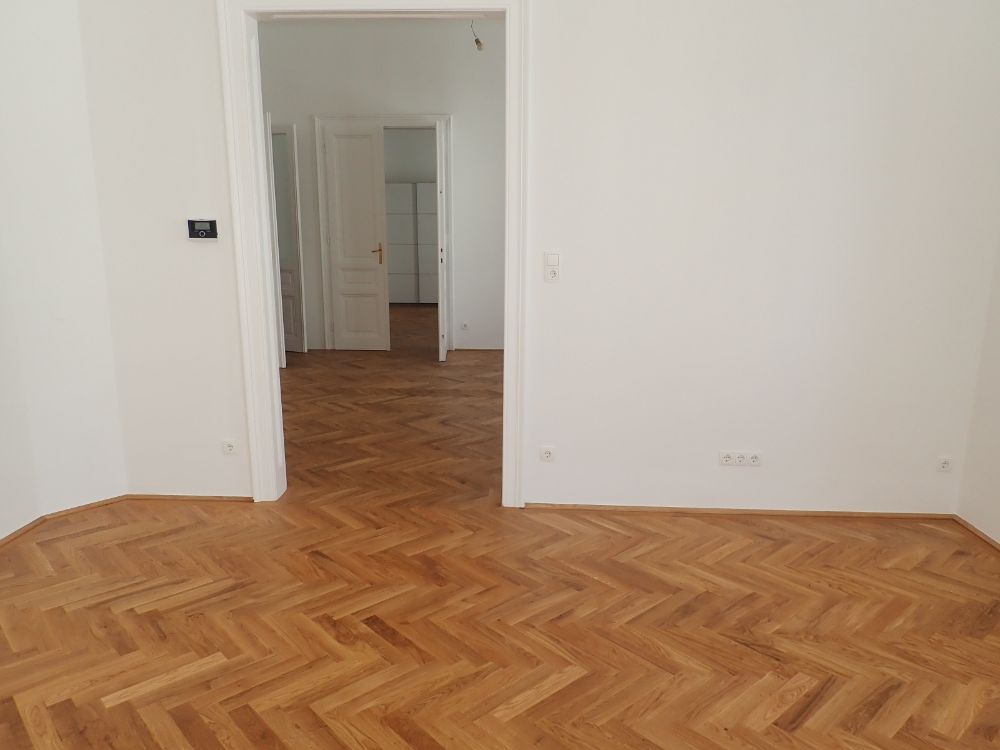 Ein leerer Raum mit Holzboden und weißen Wänden.