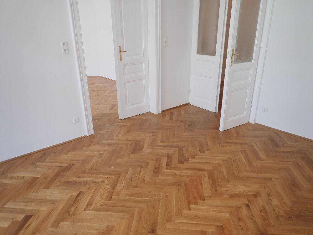 Ein leerer Raum mit Holzboden und weißen Wänden.
