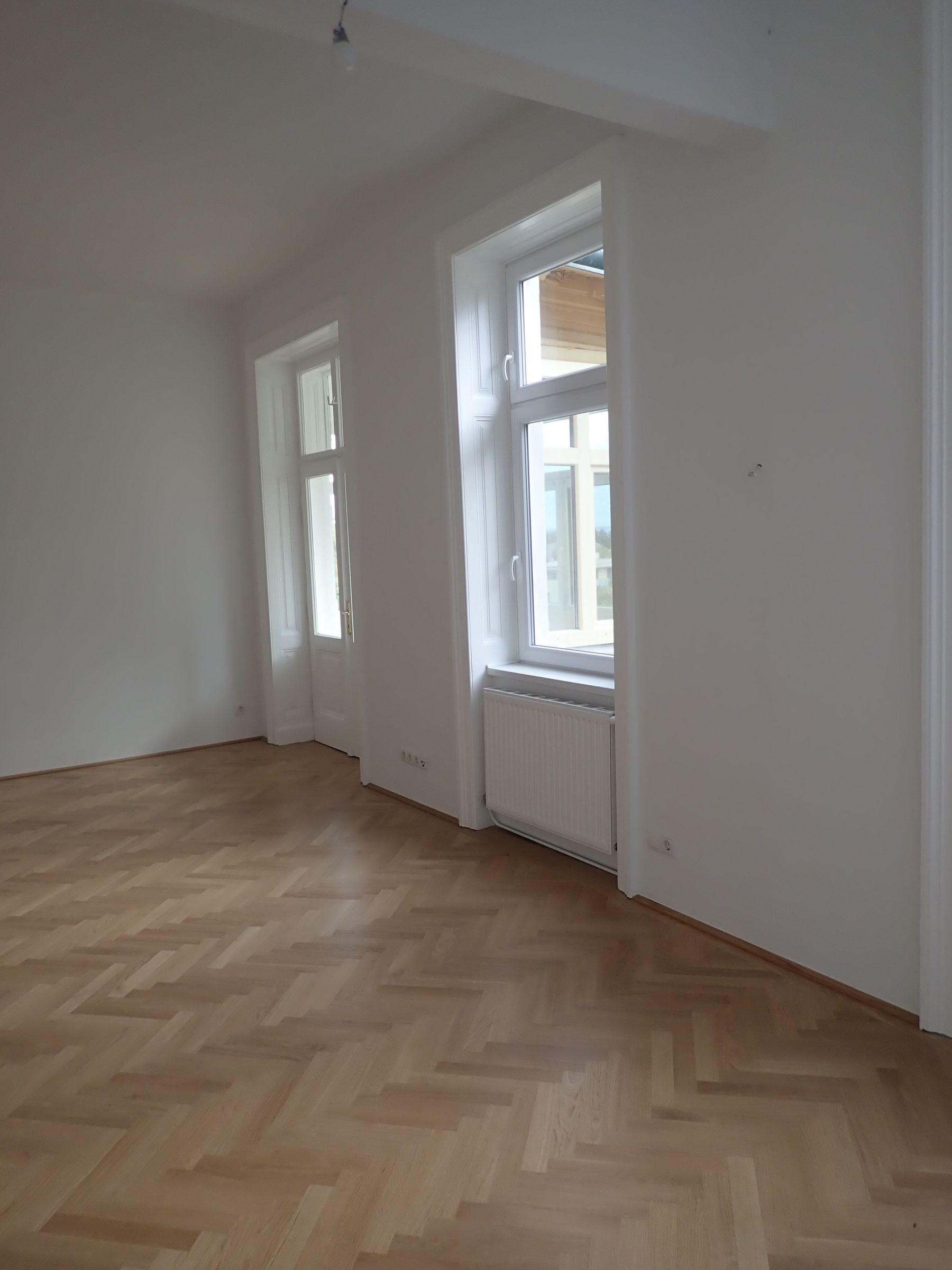 Ein leerer Raum mit Holzboden und zwei Fenstern.