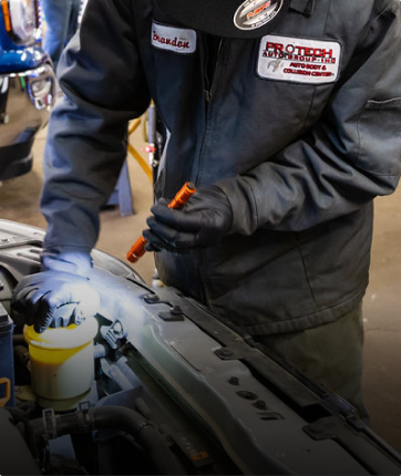 A man is working on a car with a patch on his jacket that says Protech | Protech Auto Group Inc