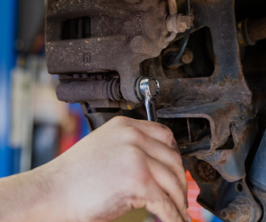 A person is working on a brake caliper with a wrench. | Protech Auto Group Inc