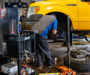 A man is working on a yellow ford truck in a garage | Protech Auto Group Inc