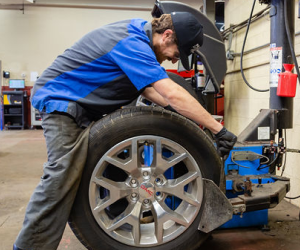 A man is balancing a tire on a machine in a garage. | Protech Auto Group Inc