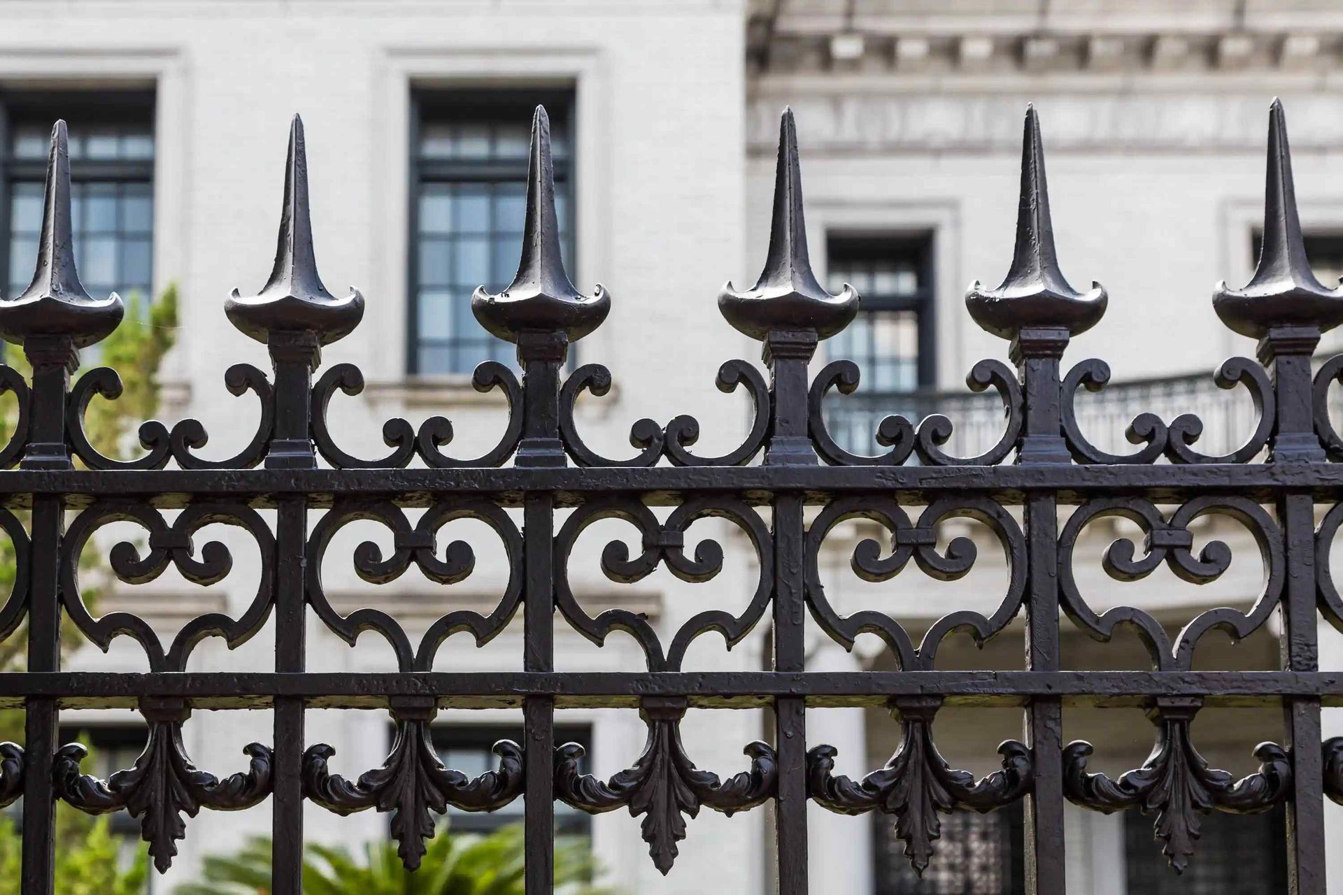 Black wrought iron fence in front of a white building with dark windows.