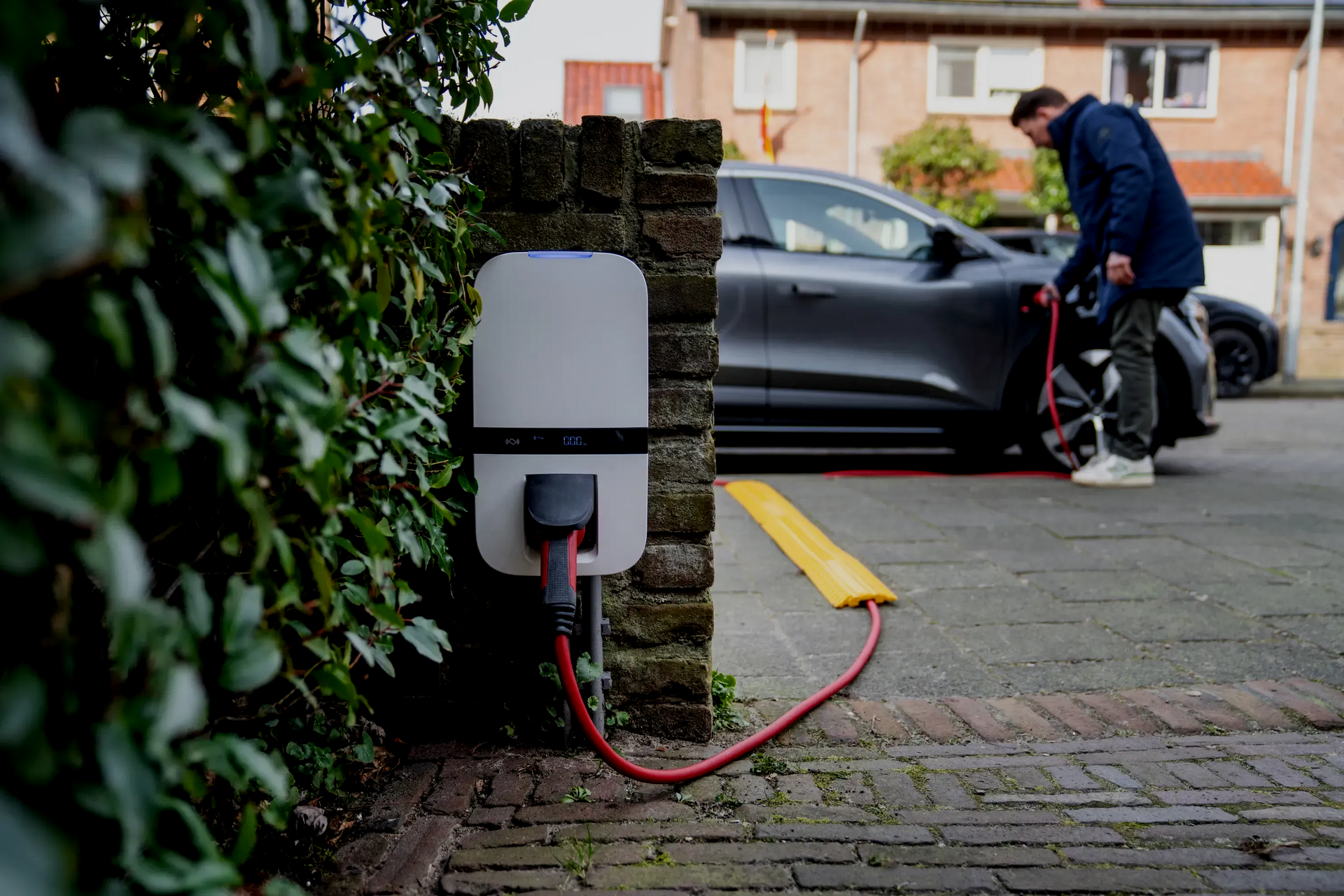 Electric vehicle charging in residential area; person plugs in car at home charger.