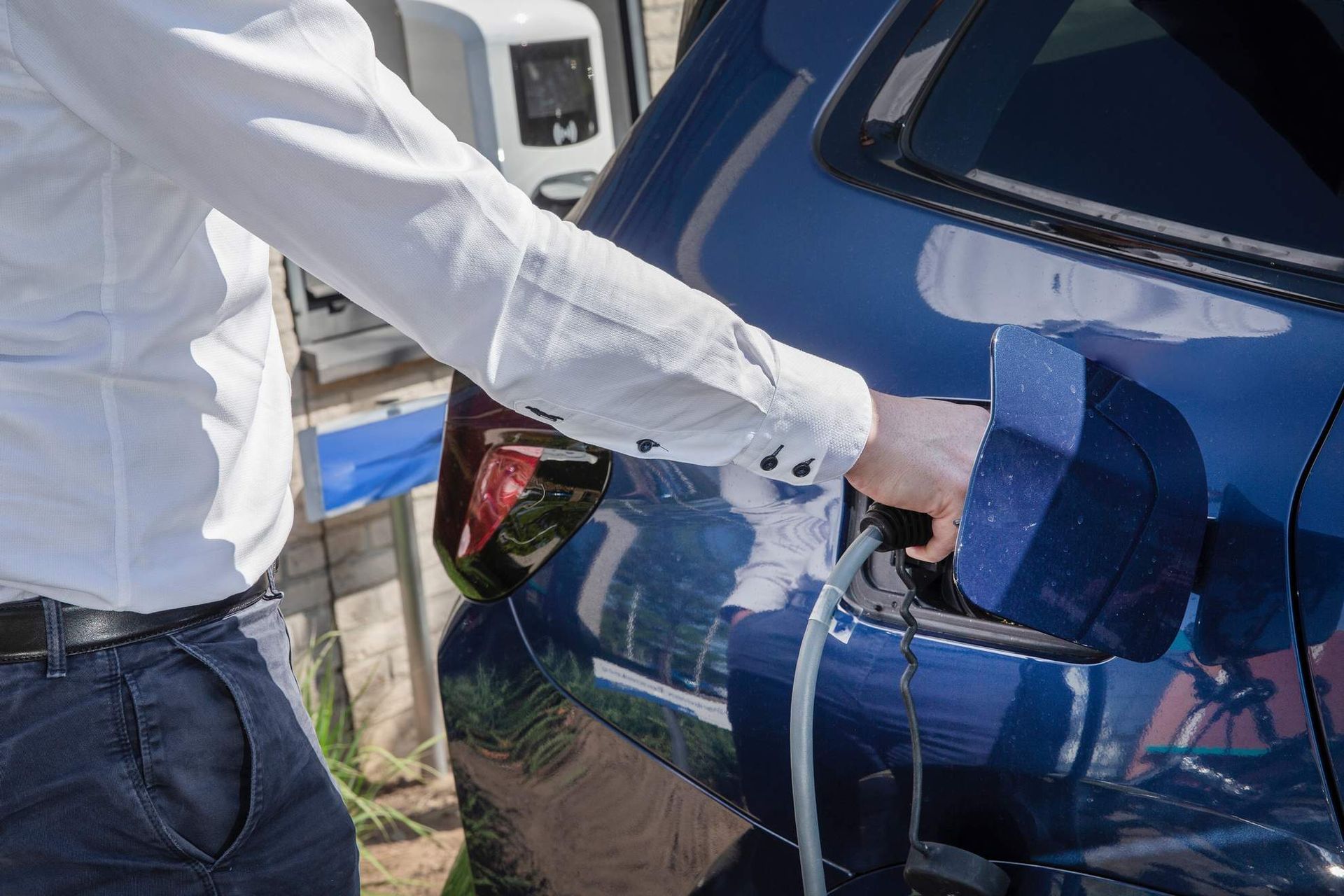 Man met sleutelhanger bij een witte elektrische auto die wordt opgeladen.