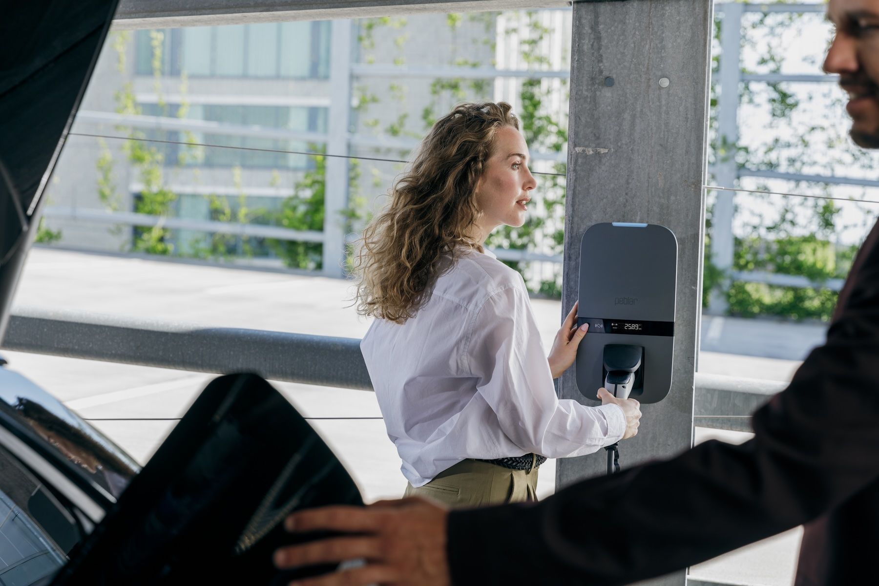 Man in een groene trui lacht terwijl hij thuis zijn elektrische auto oplaadt.