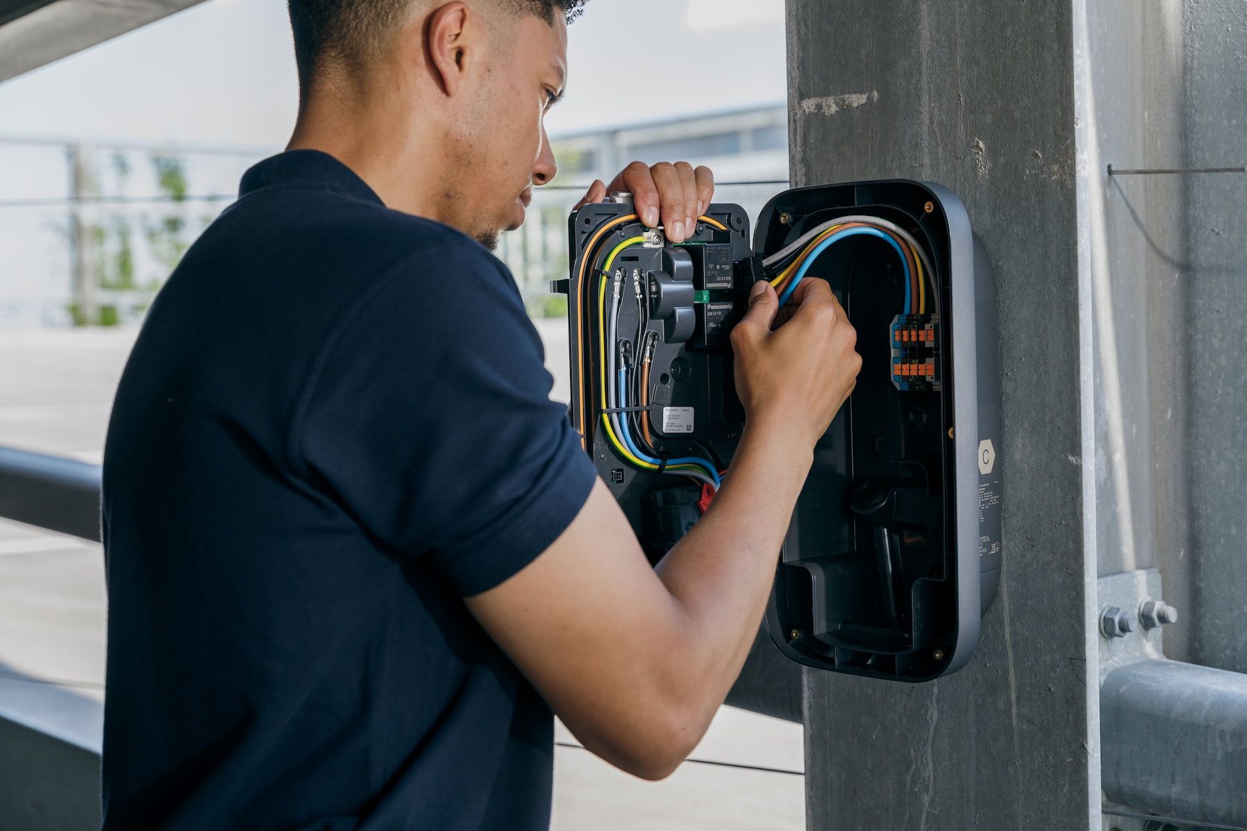 Man met afstandsbediening bij een witte elektrische auto met een oplaadkabel.