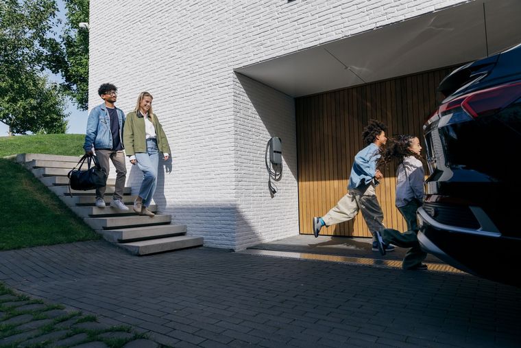Man in een groene trui lacht terwijl hij thuis zijn elektrische auto oplaadt.