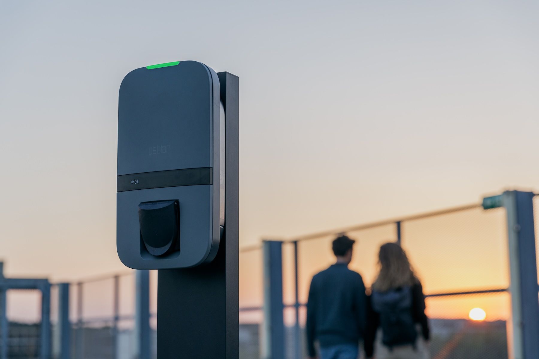 Een persoon houdt een laadstekker vast en verbindt deze met een zwart laadstation voor elektrische voertuigen.