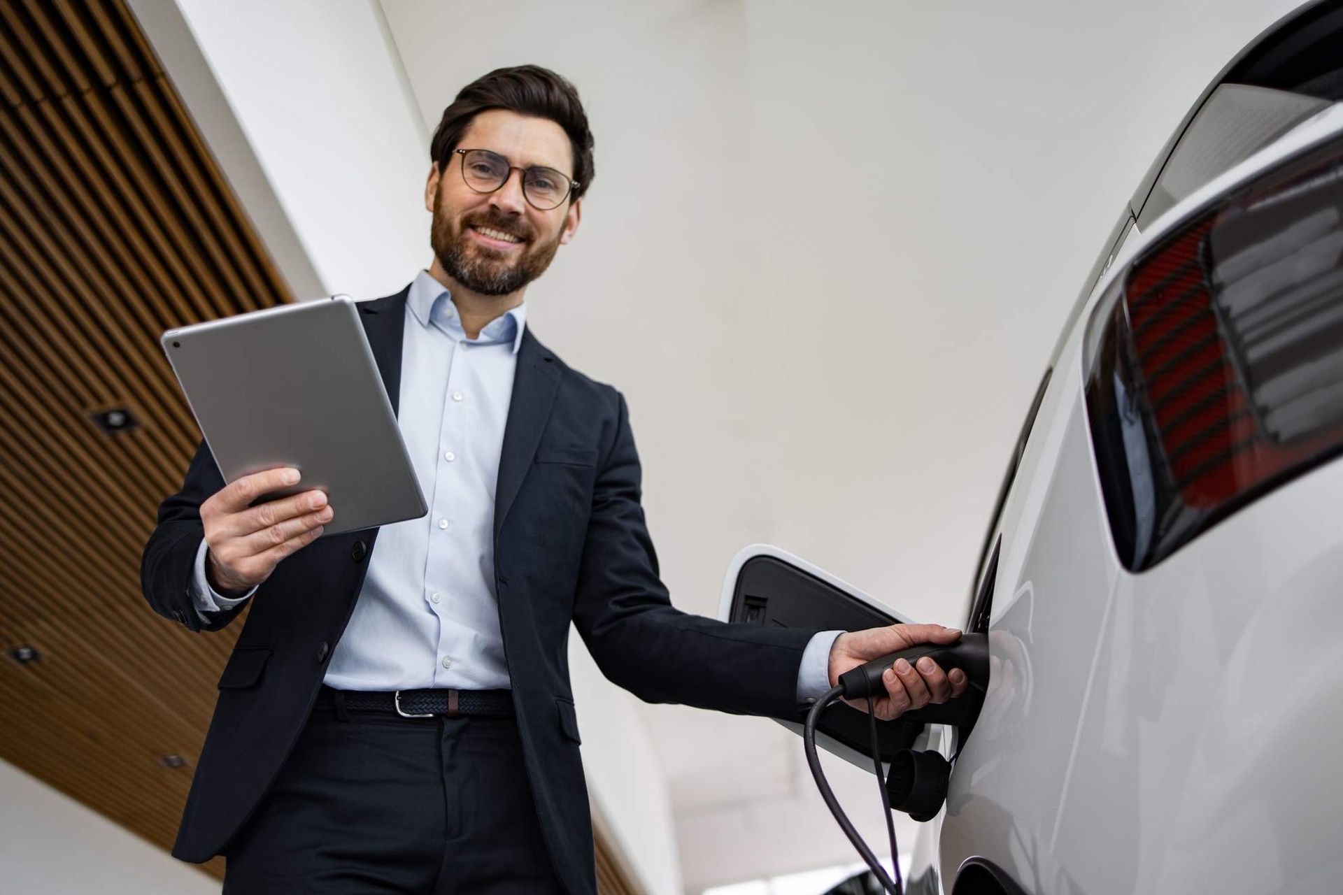 Man met sleutelhanger bij een witte elektrische auto die wordt opgeladen.