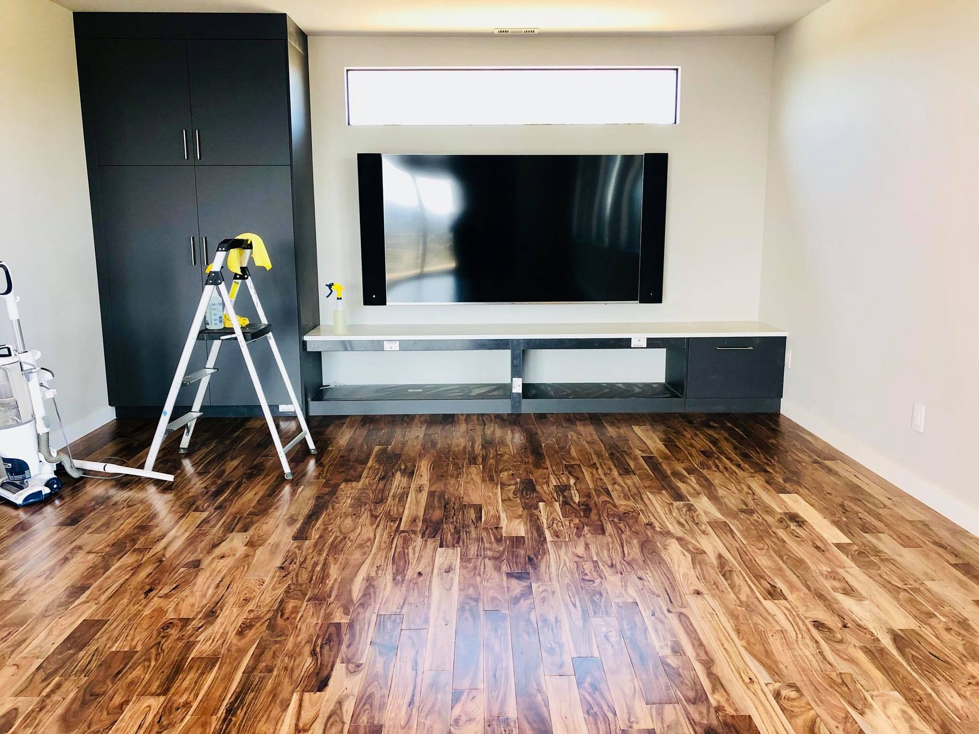 Room with dark wood floor, built-in media center, large TV, storage cabinet, and ladder.