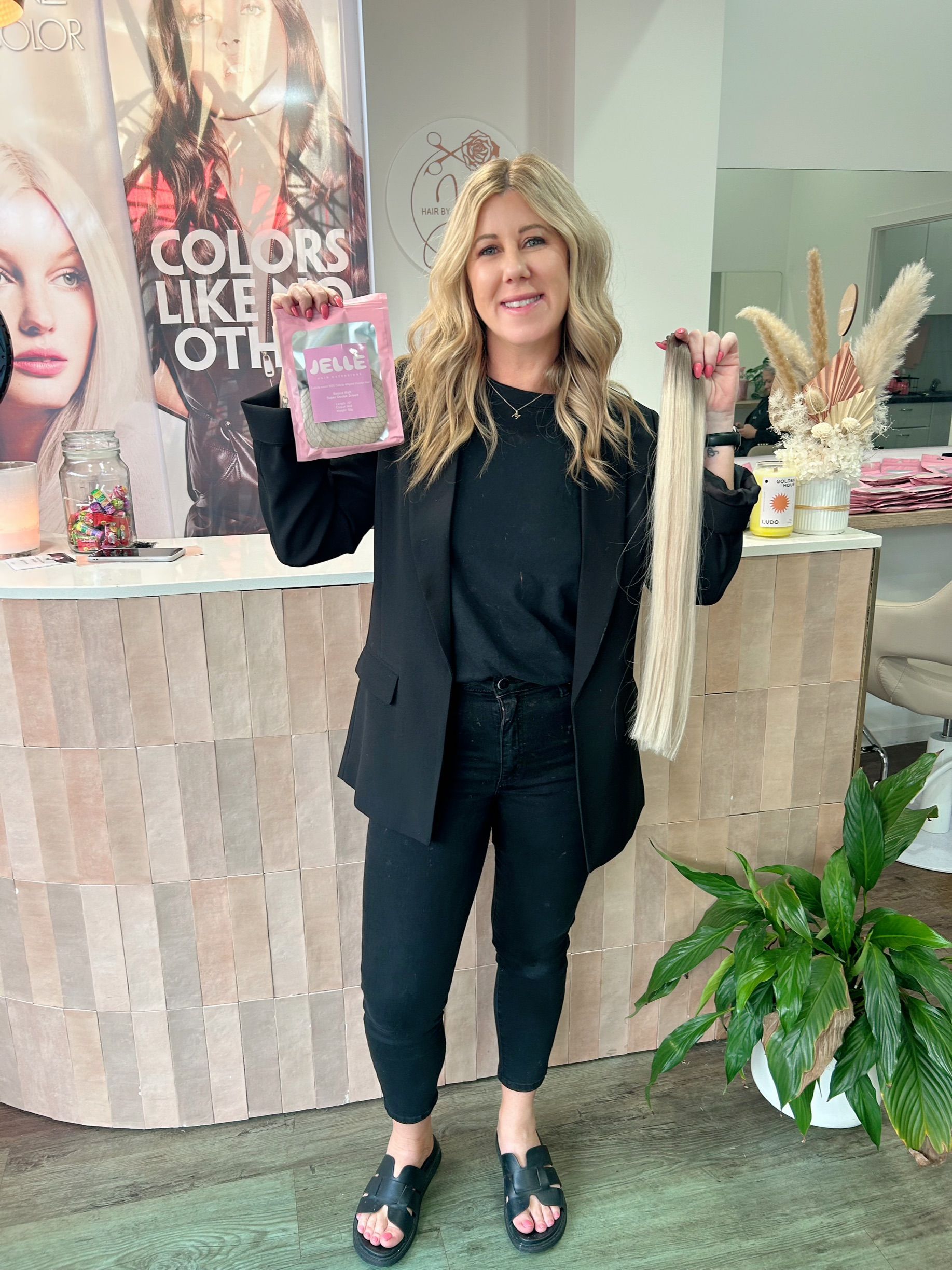 A Woman With Long Brown Hair is Standing in Front of a Sign That Says Colors Like No Other — Hair By Jell In Cannonvale, QLD