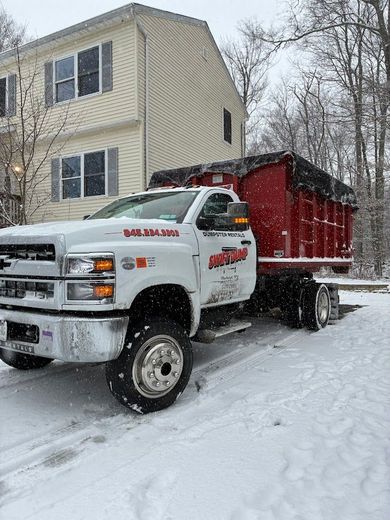 White dump truck with red bed parked in snowy driveway beside a beige house.