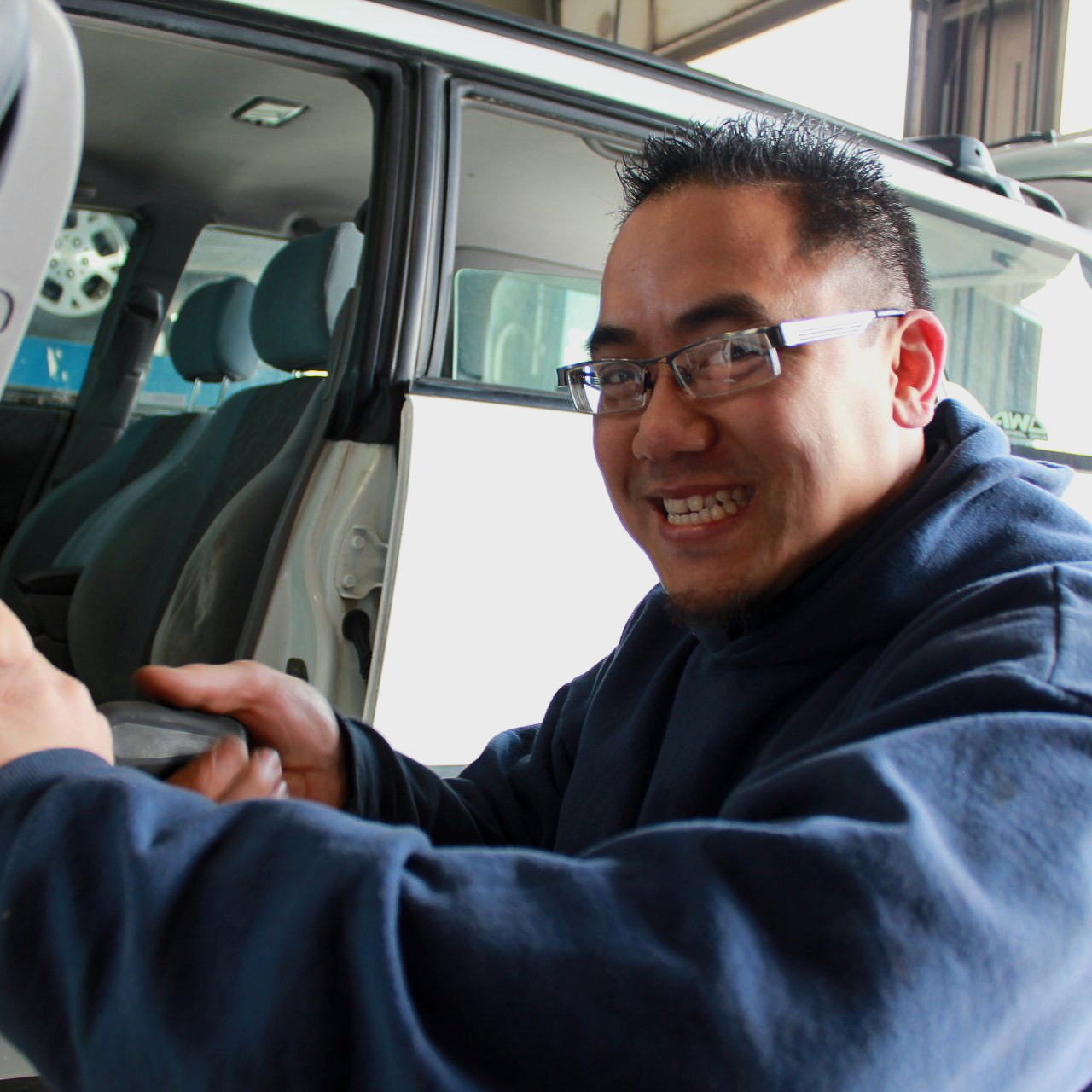A man wearing glasses is smiling while getting out of a car