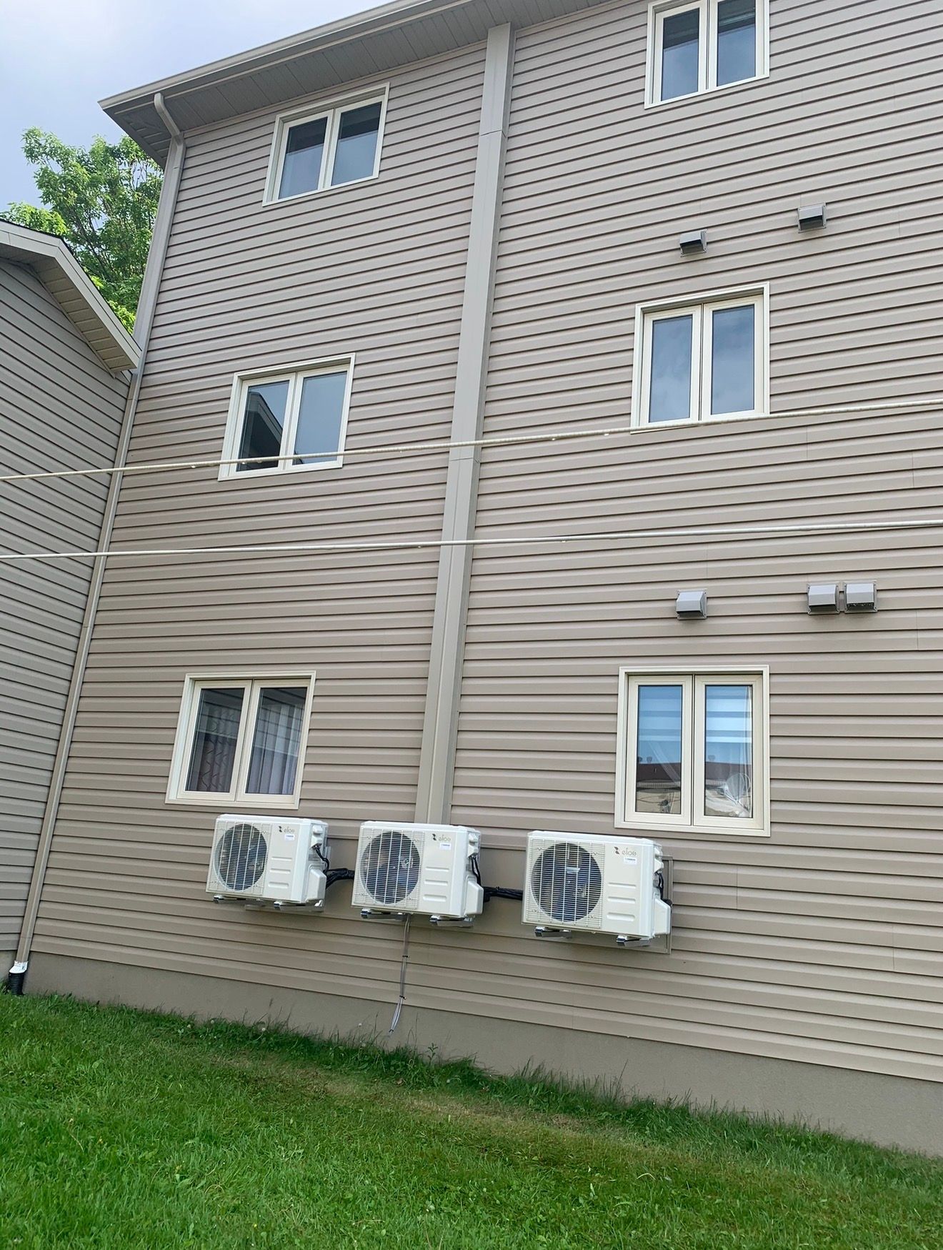 Façade du bâtiment couleur sable avec trois unités de climatisation sous les fenêtres.