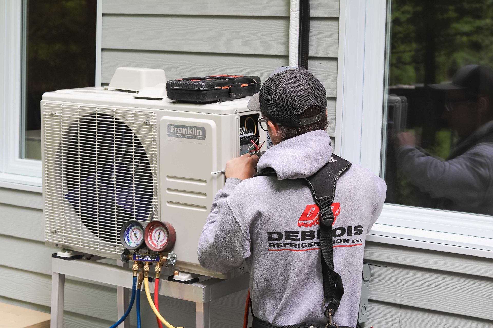 Technicien CVC travaillant sur une unité de climatisation extérieure près d'une fenêtre.