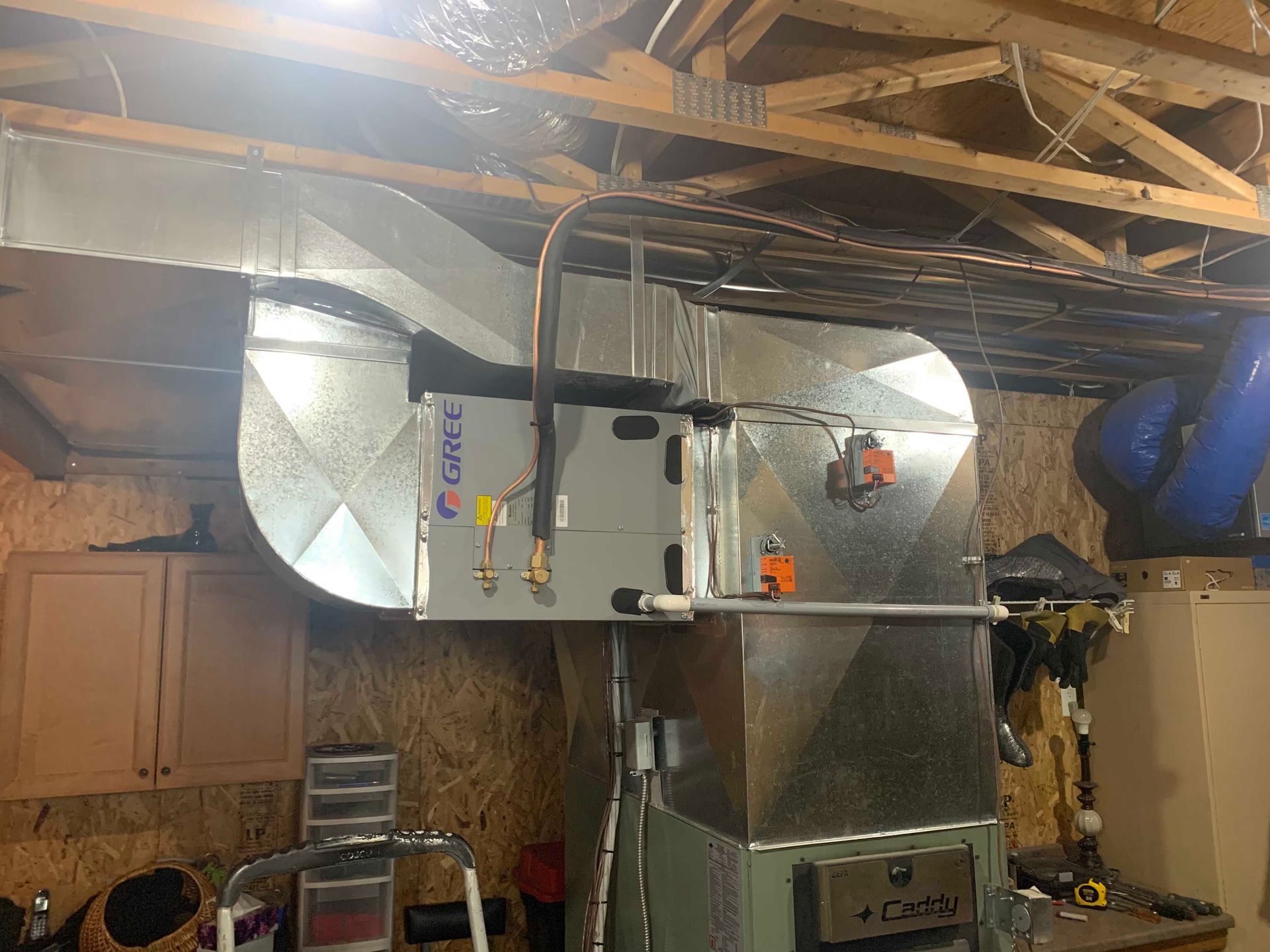 Unité de climatisation/chauffage au sous-sol, avec conduits et tuyauterie. L'unité est argentée et fixée au plafond et au mur.