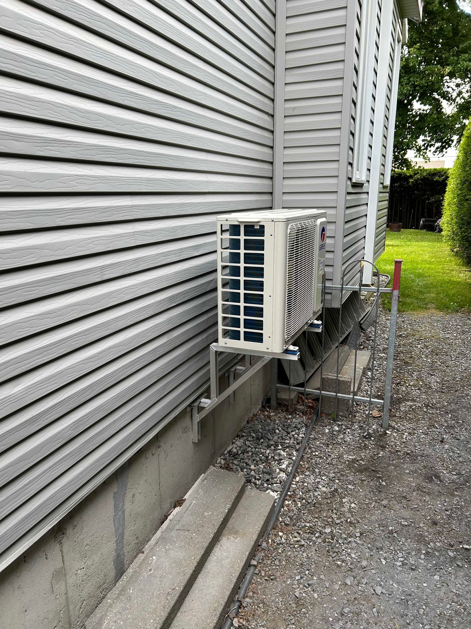 Unité de climatisation extérieure montée sur le côté d'une maison, à côté d'une fondation en béton.