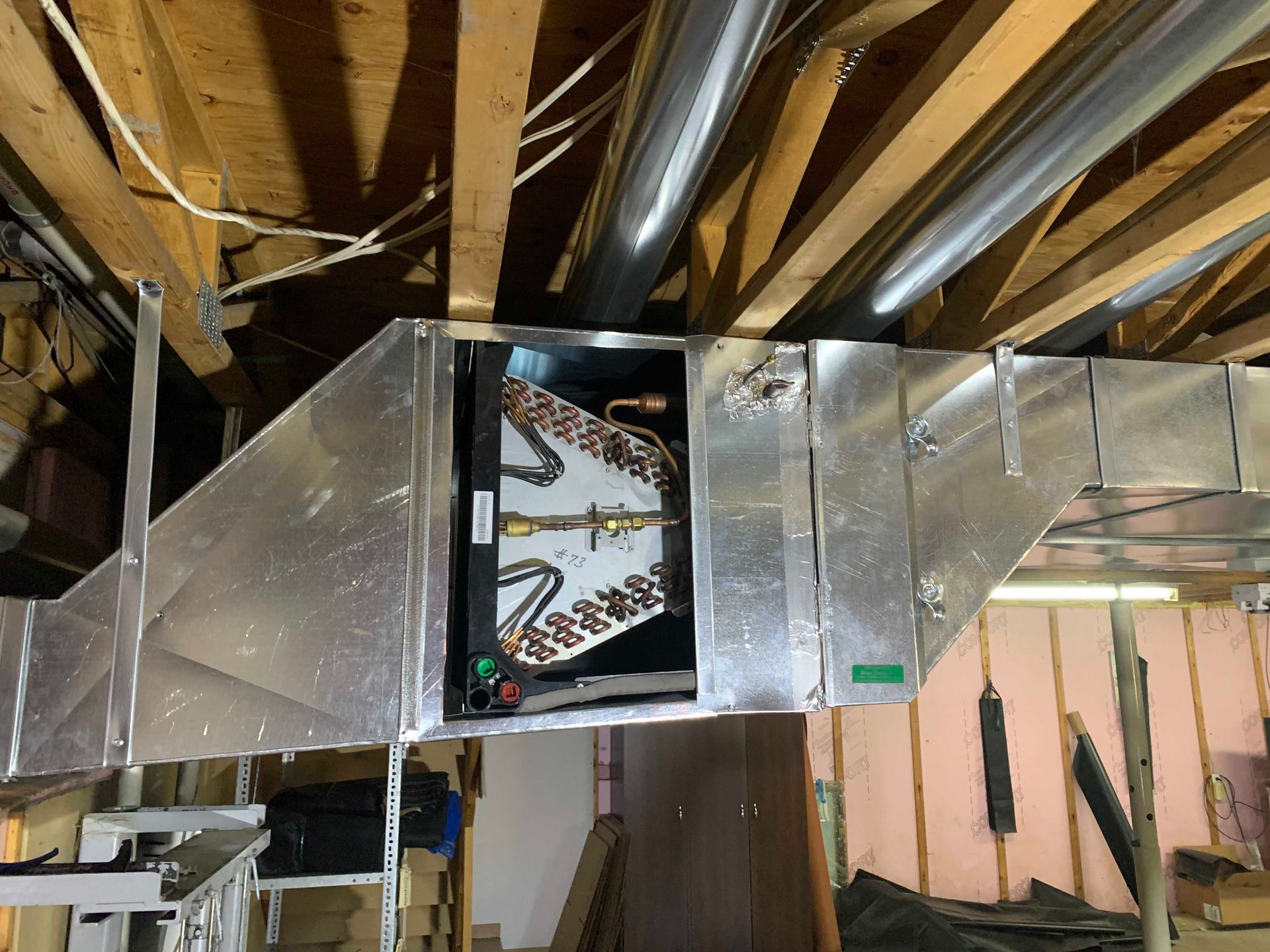 Unité de climatisation avec conduits dans un plafond de sous-sol, montrant les composants métalliques et l'isolation.