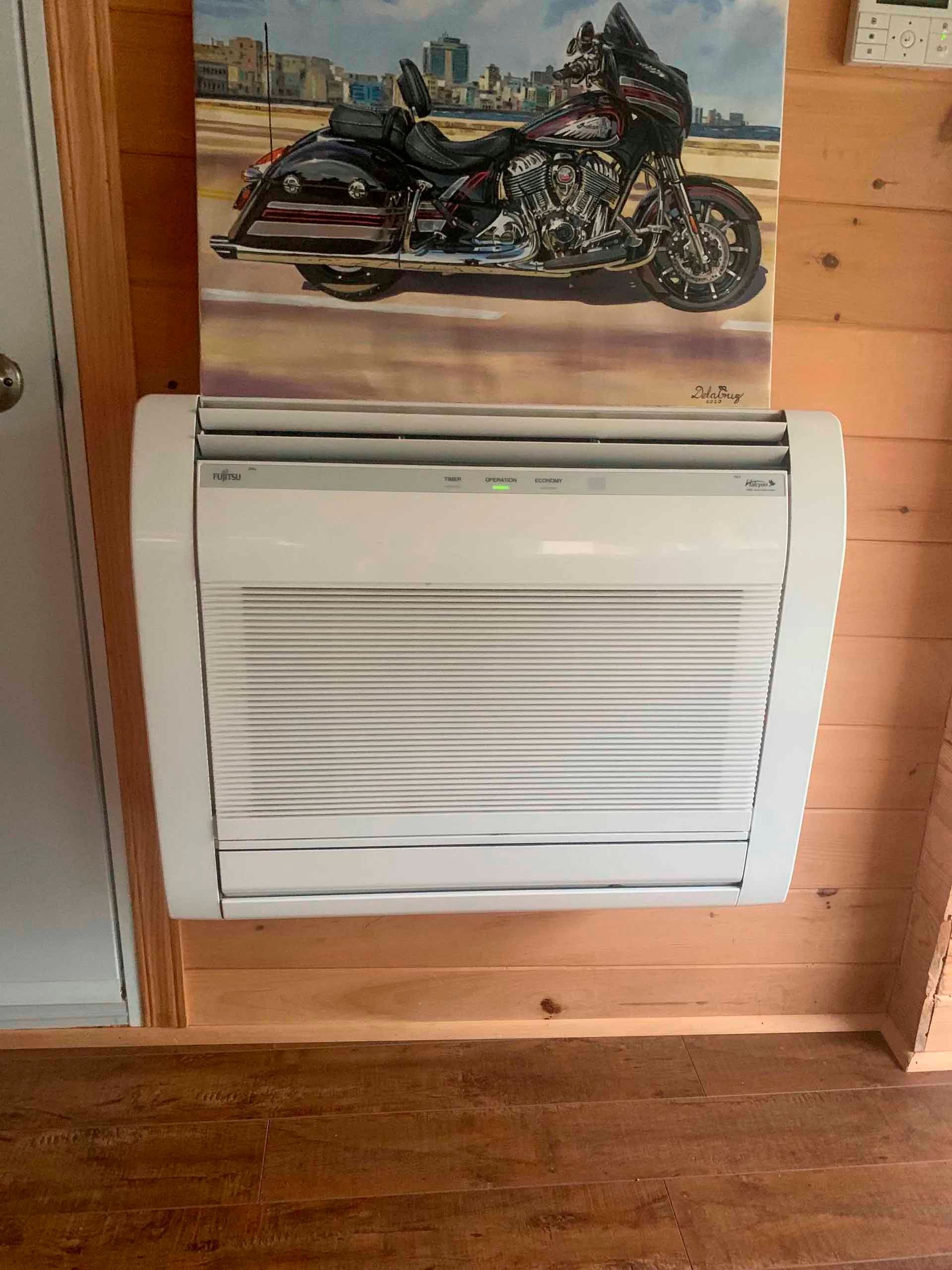 Climatiseur fixé sur un mur en bois sous un tableau de moto.