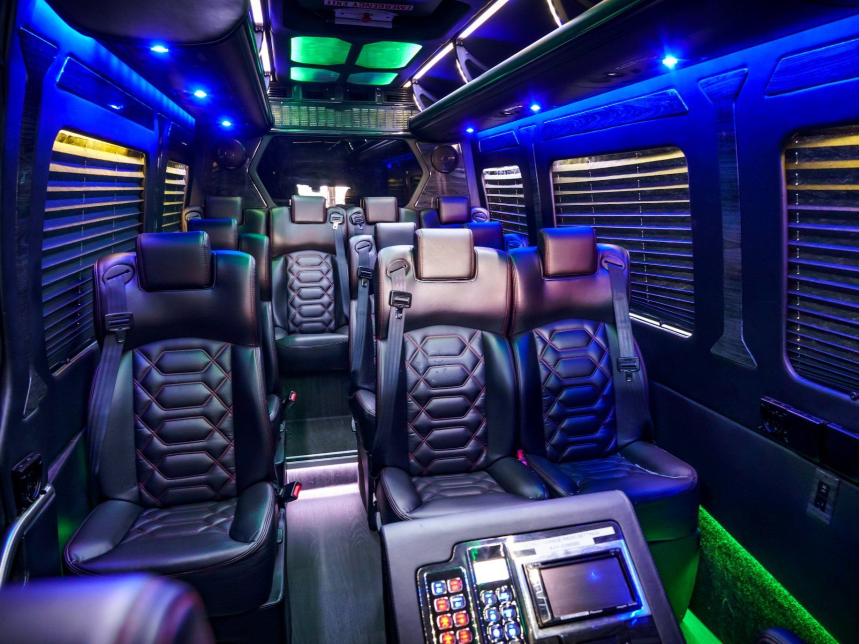 Interior of a luxury van with black leather seats, blue and green lighting, and a control panel.