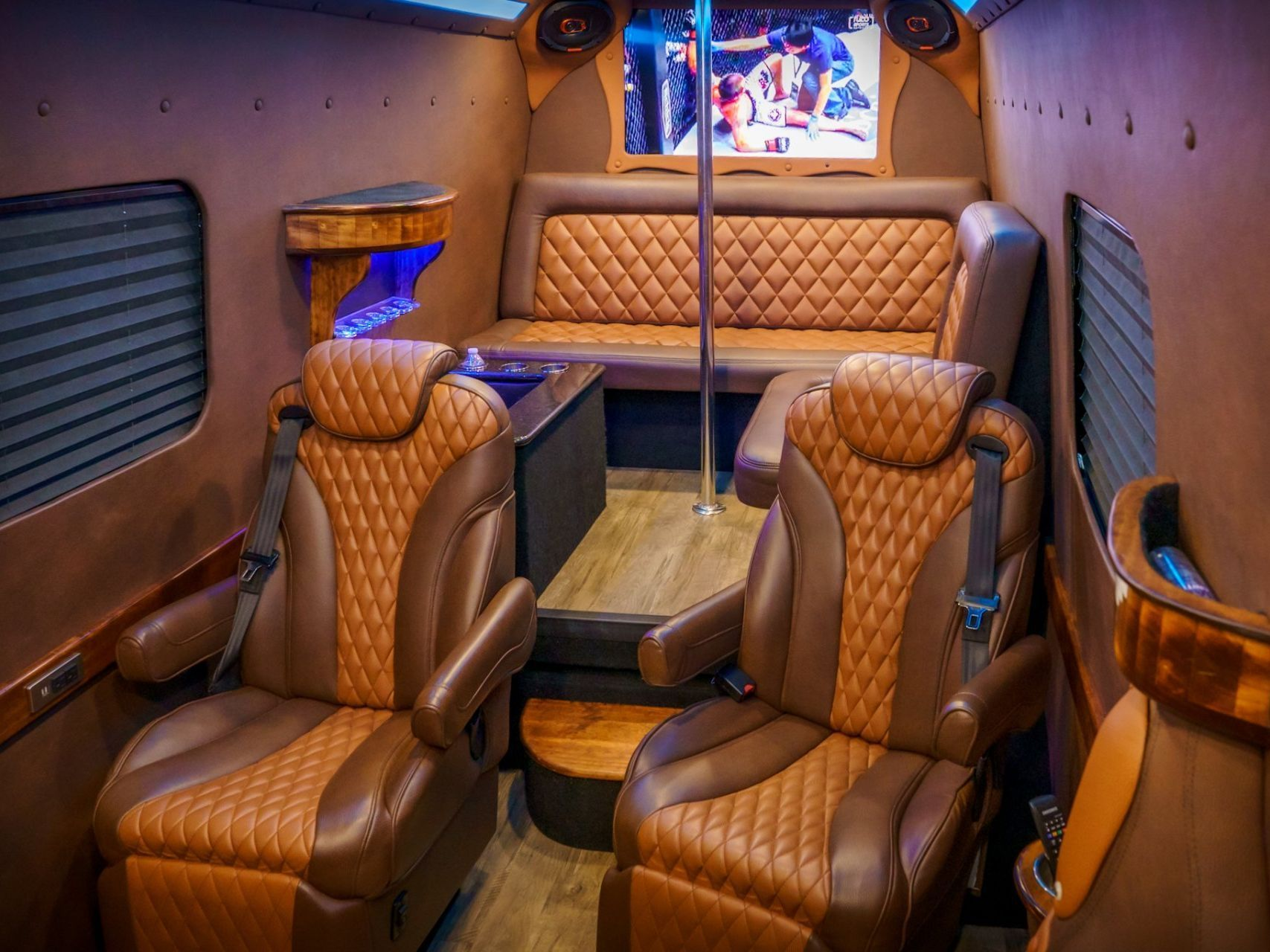 Interior of a luxury van with brown leather seats, wood paneling, a pole, and a small TV.