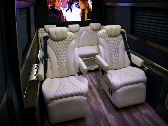 Interior of a luxury van with white quilted leather seats, a TV, and dark wood flooring.