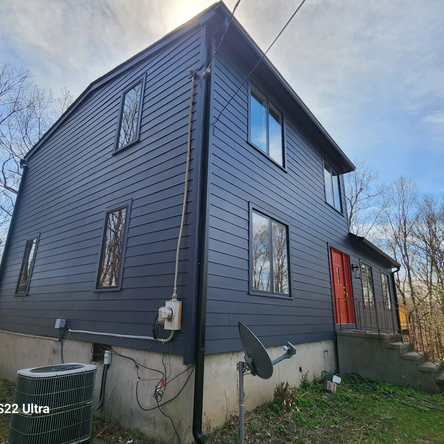 Two-story house with dark gray siding, red door, and windows.