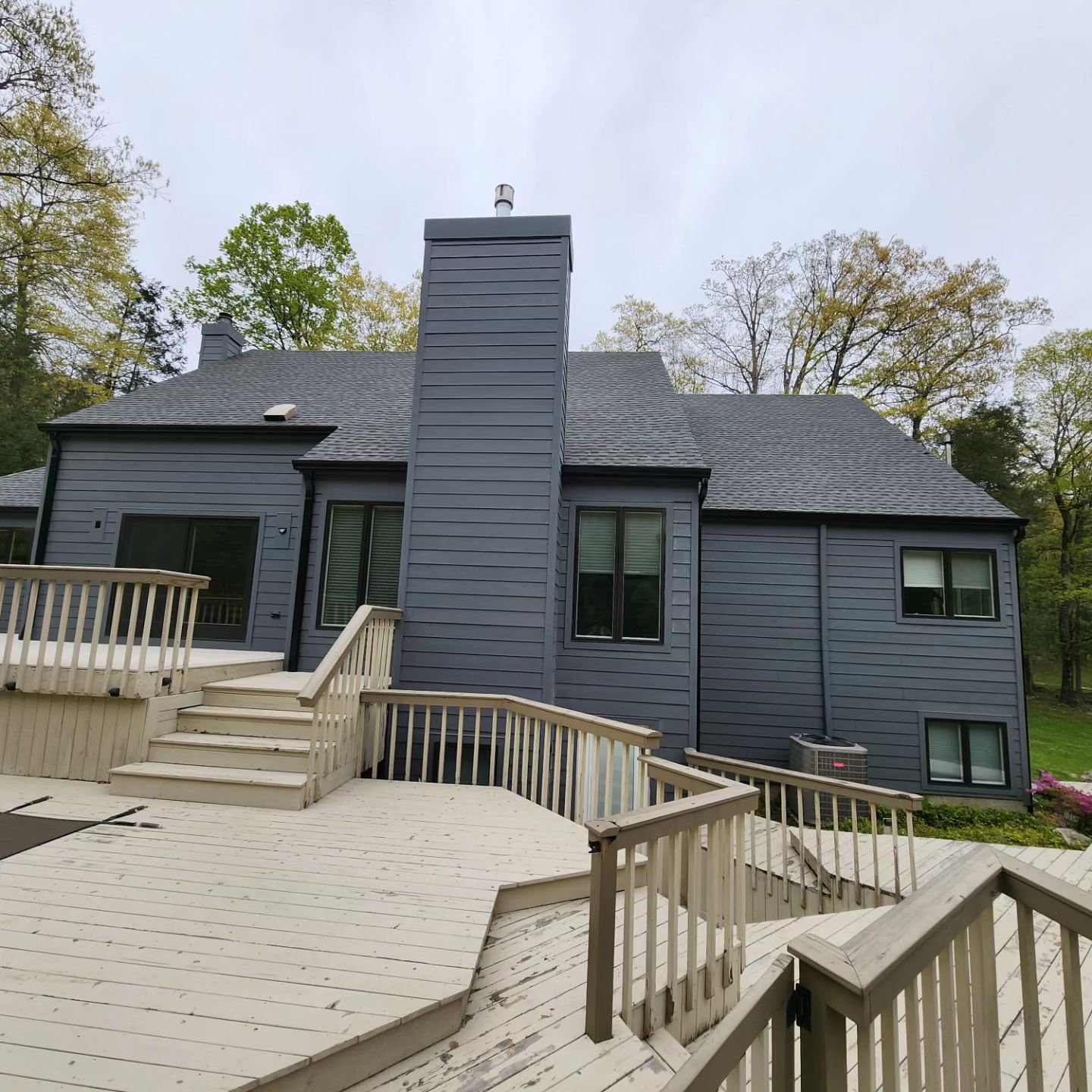 Gray house with wooden deck, chimney, windows, and surrounding trees.